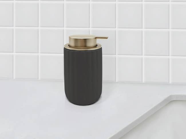 Soap dispenser with a matte decorativeness and metallic pump, acceptable against a tiled bath background