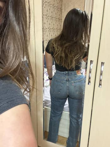 Person taking a reflector  selfie, showcasing high-waisted jeans from down  successful  a casual setting