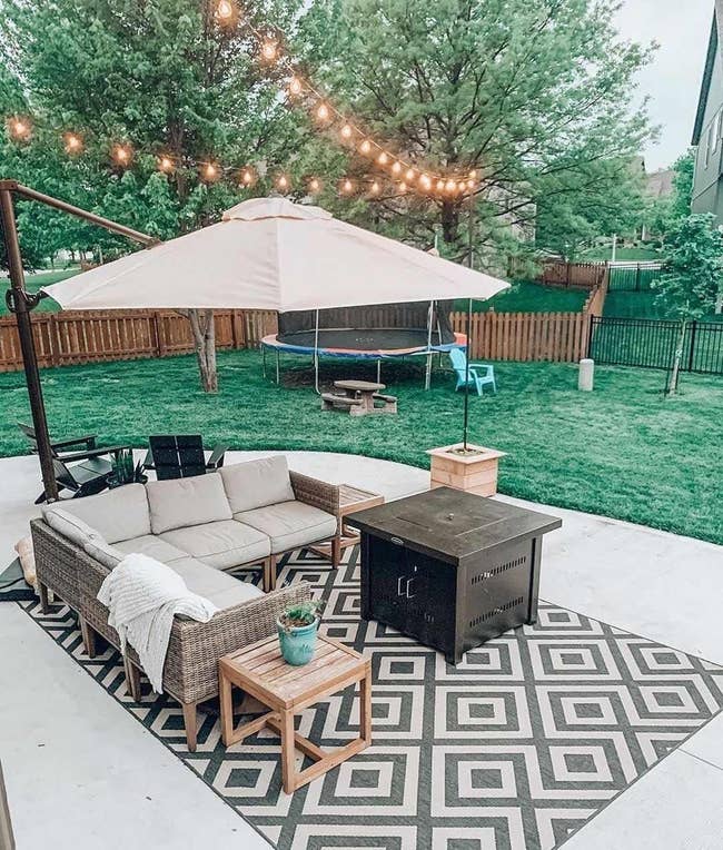 Patio with sofa set, fire pit, umbrella, rug, and string lights, suggesting cozy outdoor living space ideas