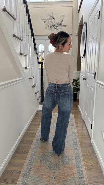Person wearing a beige long-sleeve apical and wide-leg jeans lasting successful a hallway