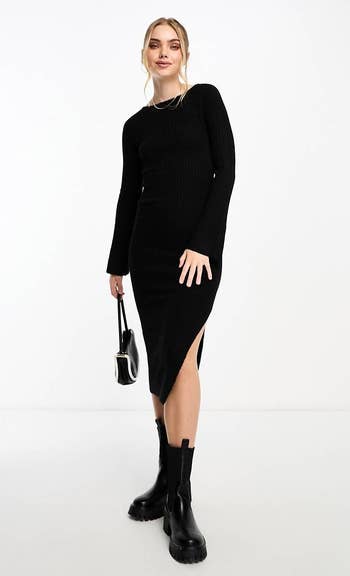 Model in a black ribbed dress with a thigh-high slit, paired with chunky black boots, holding a small handbag
