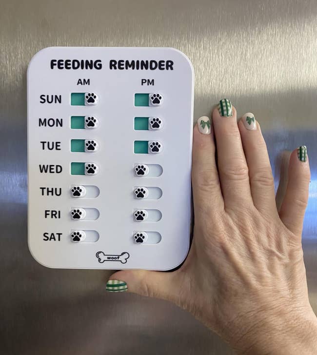Hand showing a play favored feeding reminder with checkboxes for AM and PM feedings, indicating completed days with paw prints