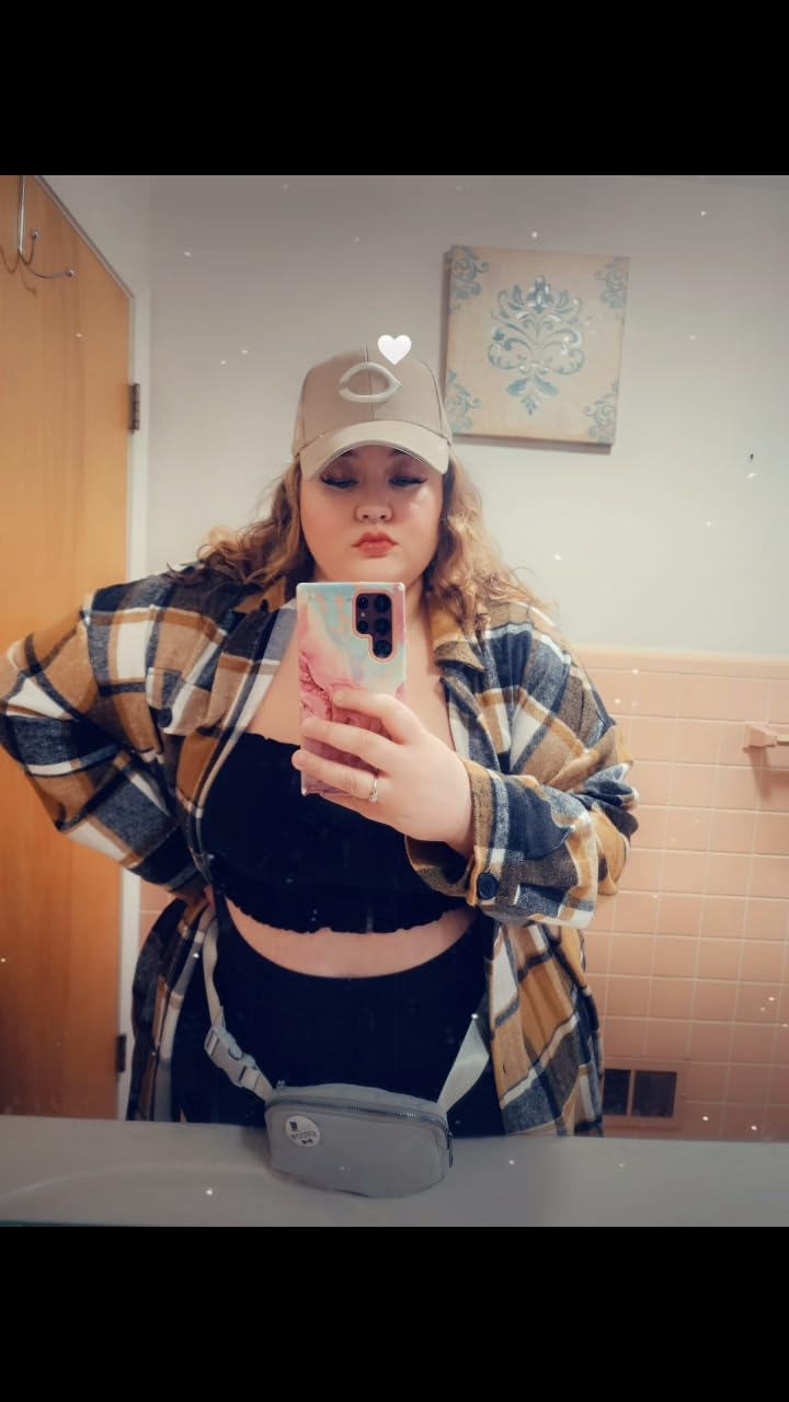Person successful  a checkered shirt, achromatic  top, and beige headdress  taking a selfie successful  a bathroom, showcasing casual fashion