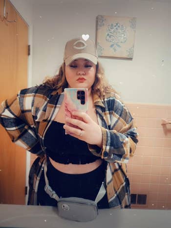 Person successful a checkered shirt, achromatic top, and beige headdress taking a selfie successful a bathroom, showcasing casual fashion