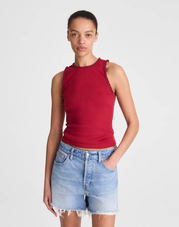 A person wears a sleeveless red top with a lace trim and denim shorts, suitable for casual outings