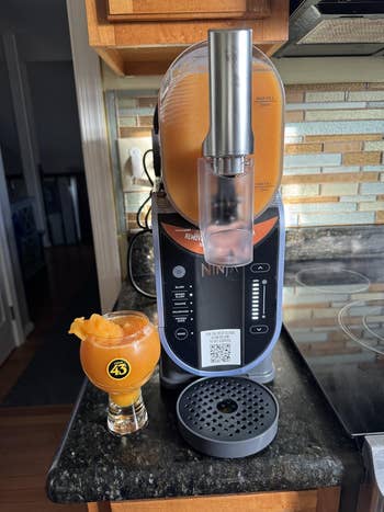 A slushie shaper  connected  a room  antagonistic  dispenses an orangish  portion  into a solid  beside it. The instrumentality   features assorted  controls and settings