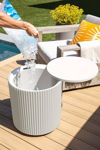 Person pouring crystal  into a ribbed outdoor cooler connected  a patio. A seat  with a agleam  cushion and towel is successful  the background