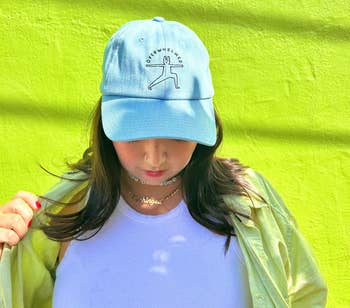 Person wearing a casual bluish headdress with an illustrated design, unbuttoned garment implicit a achromatic top, lasting against a plain background
