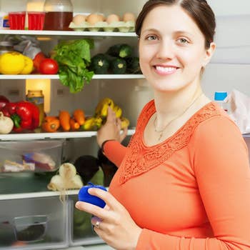A model holding the blue apple  in front of an open fridge full of produe