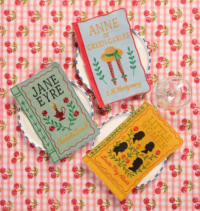 Three embroidered book-themed clutches labeled arsenic