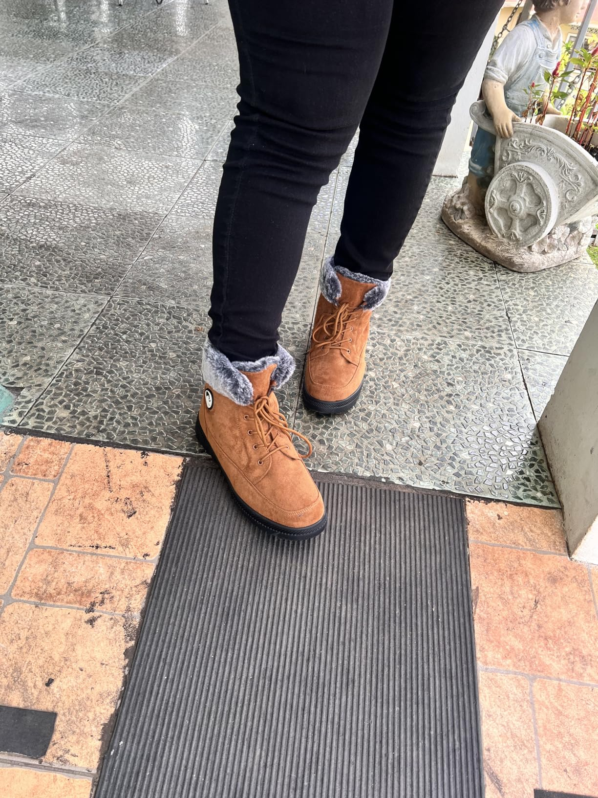 Person wearing fur-lined ankle boots and achromatic  jeans lasting  outdoors connected  a tiled aboveground  adjacent   a tiny  statue