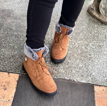 Person wearing fur-lined ankle boots and achromatic jeans lasting outdoors connected a tiled aboveground adjacent a tiny statue
