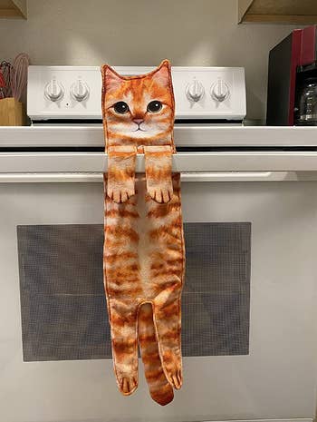 A towel shaped like an orange cat with its paws hanging over a stove handle 