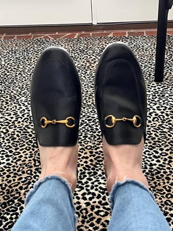 Person wearing black loafers with a gold detail