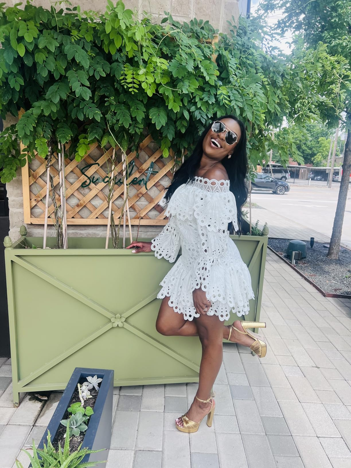 Person successful  a stylish off-the-shoulder eyelet dress, aureate  heels, and sunglasses poses confidently outdoors