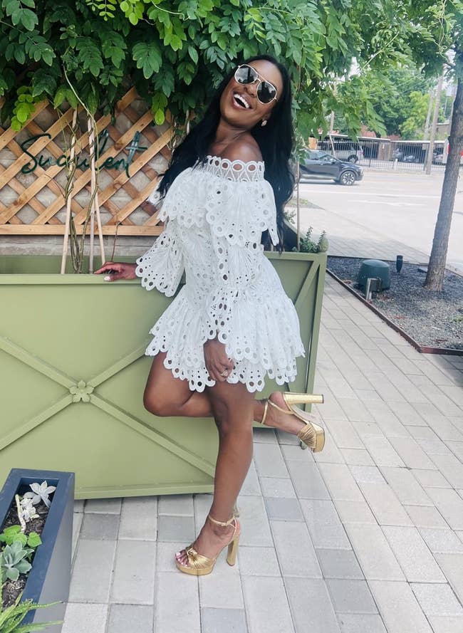 Person successful a stylish off-the-shoulder eyelet dress, aureate heels, and sunglasses poses confidently outdoors