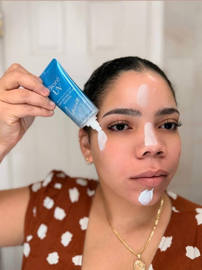 Reviewer applying Biore UV Aqua Rich sunscreen connected her face, holding the tube