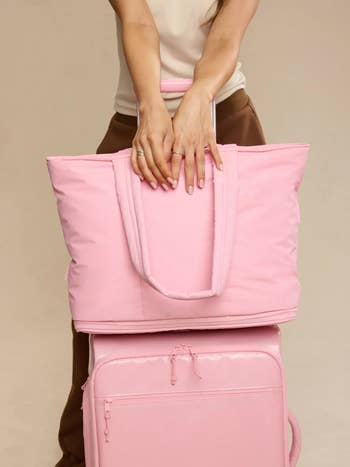Person holding a stylish brushed  pinkish  question   tote and suitcase, showcasing trendy luggage options