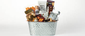 Metal basket filled with popcorn, gourmet pretzels, crackers, cheese spread, mustards, and assorted snack items
