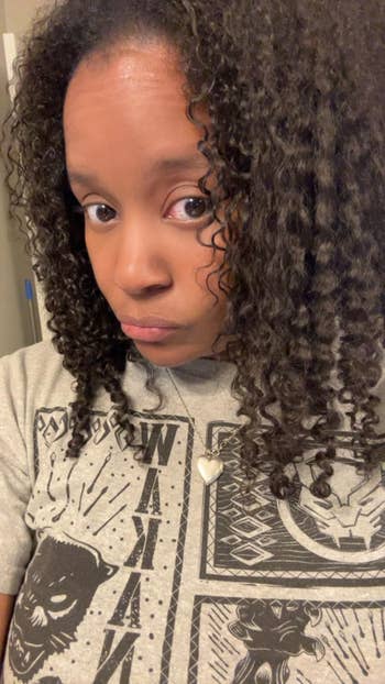 Person wearing a graphic T-shirt with bold patterns, curly hair, and a pendant necklace takes a selfie