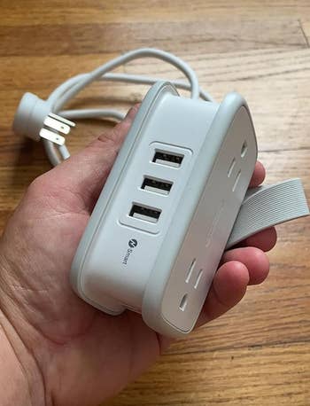 A manus  holding a multi-port powerfulness  portion   with USB outlets, against a woody  background