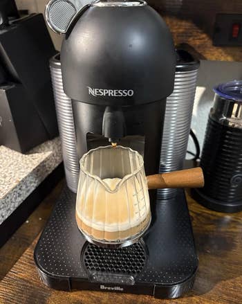 Nespresso instrumentality   brewing java  into a solid  pitcher with a woody  handle, placed connected  a room  counter