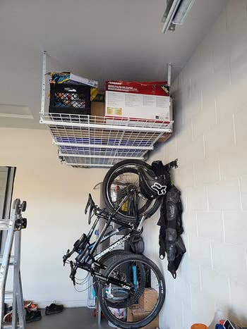 reviewer's white ceiling mount shelves installed in garage holding boxes and other items with bike rack on wall under it