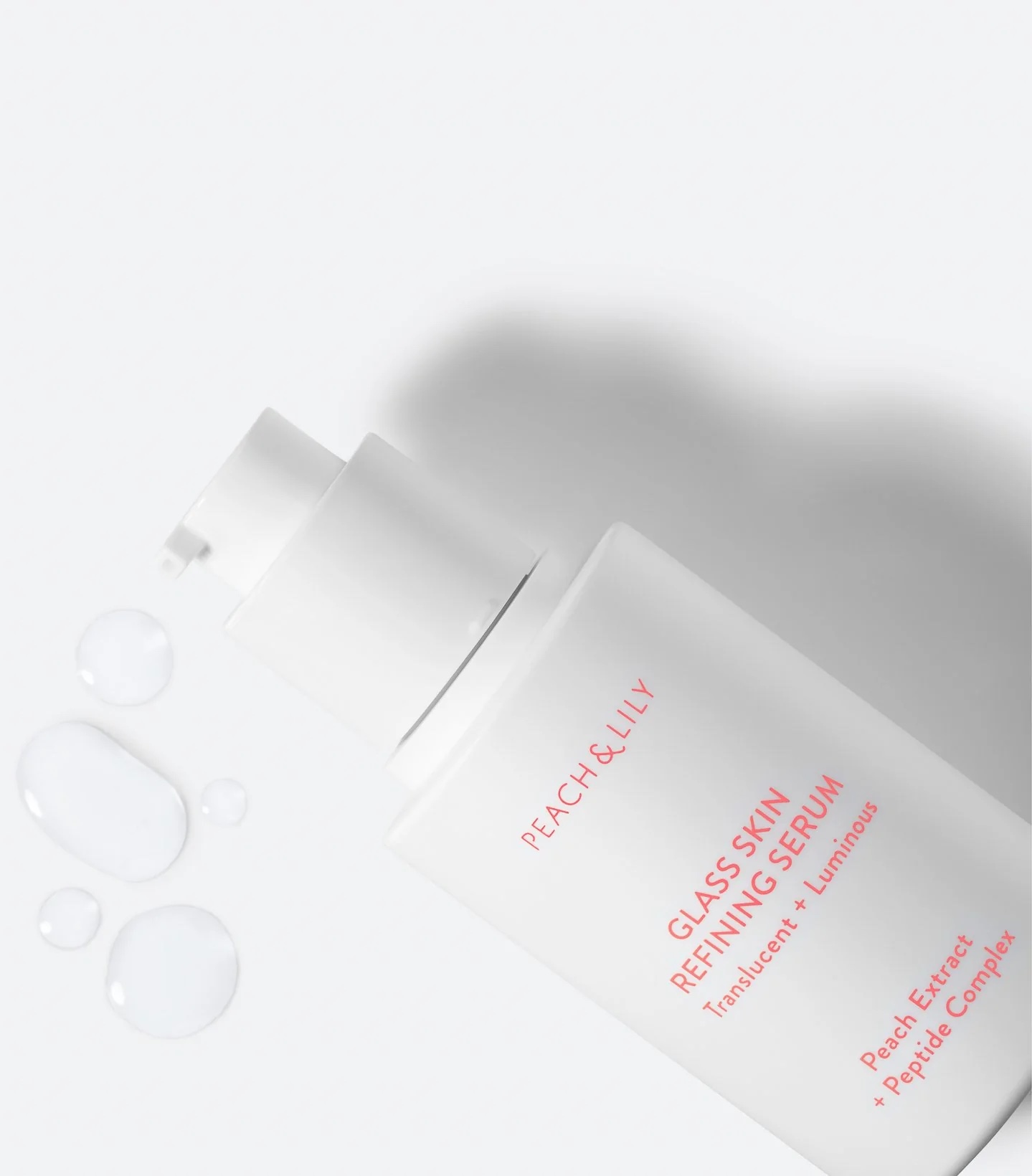 the white bottle of serum with pink lettering next to a few drops of the clear serum