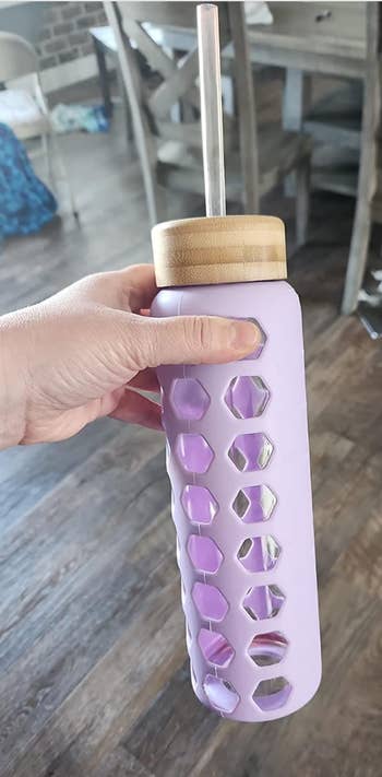 a reviewer holding the purple bottle with hexagon cut outs and a bamboo lid with straw