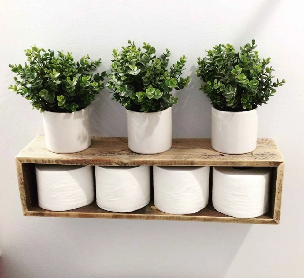 Wooden rectangular wall mounted shelf with toilet paper inside and there plants on top