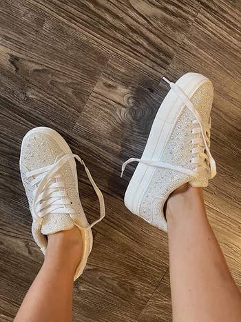 reviewer photo of them wearing a pair of rhinestone- and faux pearl-encrusted white sneakers