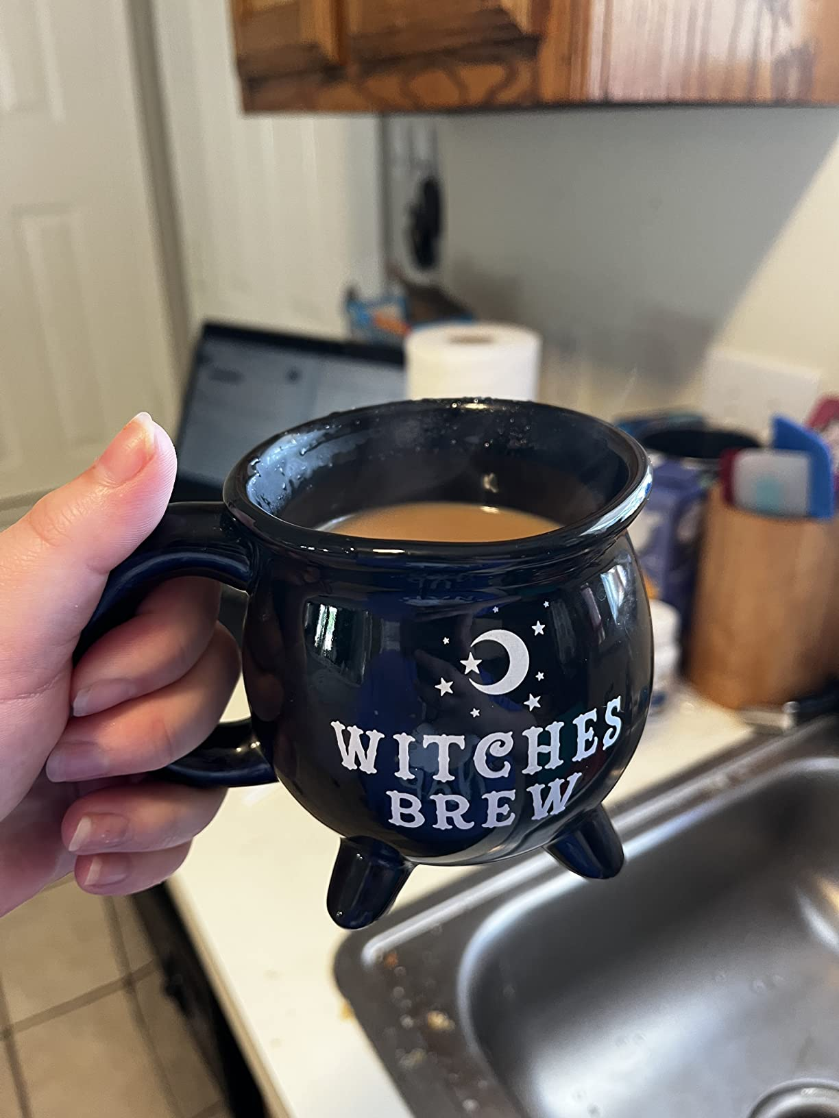 Person holding a achromatic  cauldron-shaped mug labeled 