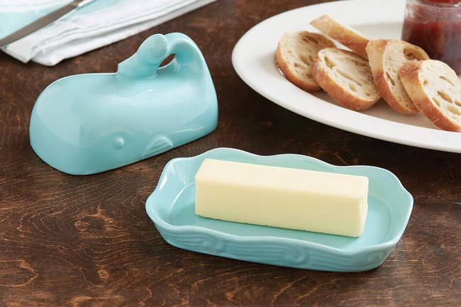 Whale-shaped butter dish on a table with a stick of butter on it and sliced bread on a plate nearby