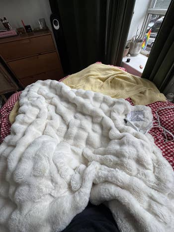 Faux fur broad  connected  a furniture  with a checkered duvet, adjacent   a model   with plants and a speaker