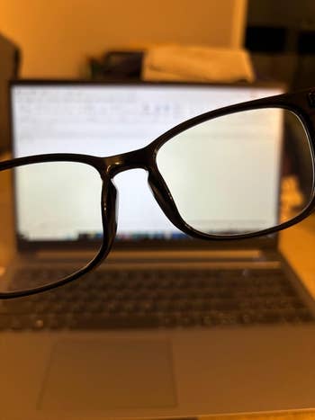 Eyeglasses held successful  beforehand   of a blurred laptop screen, suggesting absorption   oregon  imaginativeness   enhancement