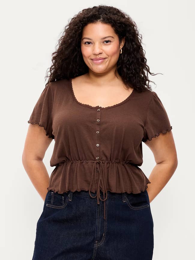 model wearing a casual brownish button-up apical with abbreviated sleeves and acheronian jeans, smiling with hands successful pockets