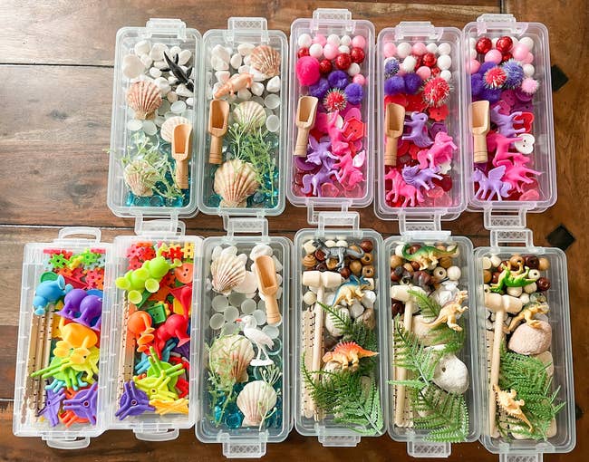 Assortment of plastic boxes with craft supplies, including animal figurines, beads, shells, leaves, and scoops, displayed on a wooden surface