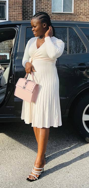 Reviewe successful  a pleated knee-length formal  and strappy heels stands beside a car, holding a studded handbag