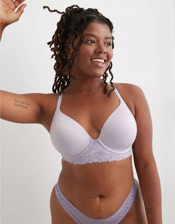 Model in a lavender lace-trimmed bra with matching underwear, smiling, hand raised
