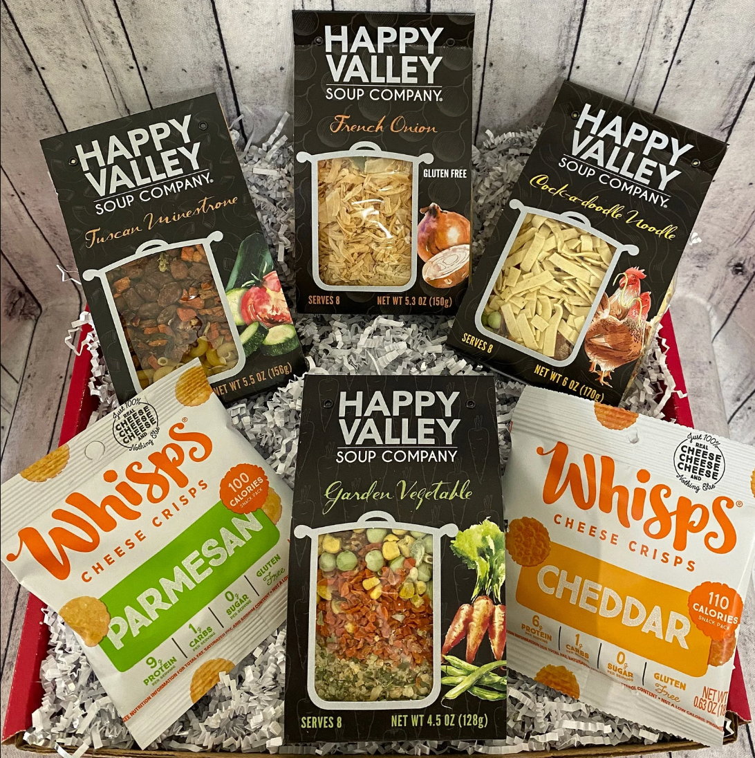 Red box with two bags of cheese crips and four bags of dried soup on a wooden background