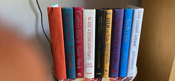 Books lined up connected a shelf, including titles by Patterson, Robb, and Demille, suitable for buying nonfiction connected fashionable authors