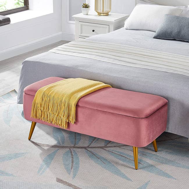 a pink storage bench in front of a bed 