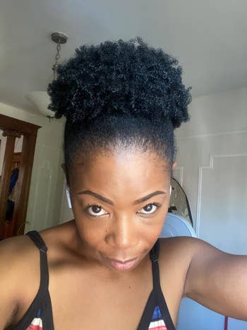a reviewer with tight coils wearing their hair in a puff