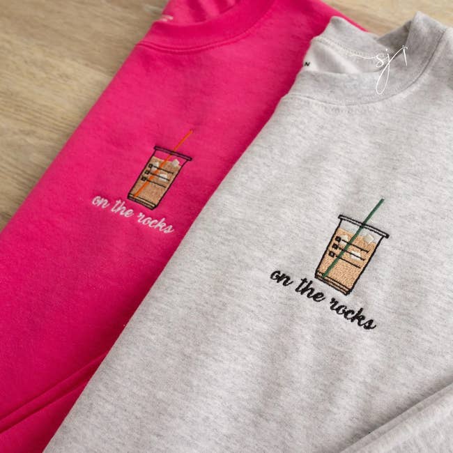 a pink sweatshirt and a gray sweatshirt each with an iced coffee embroidered on it and 