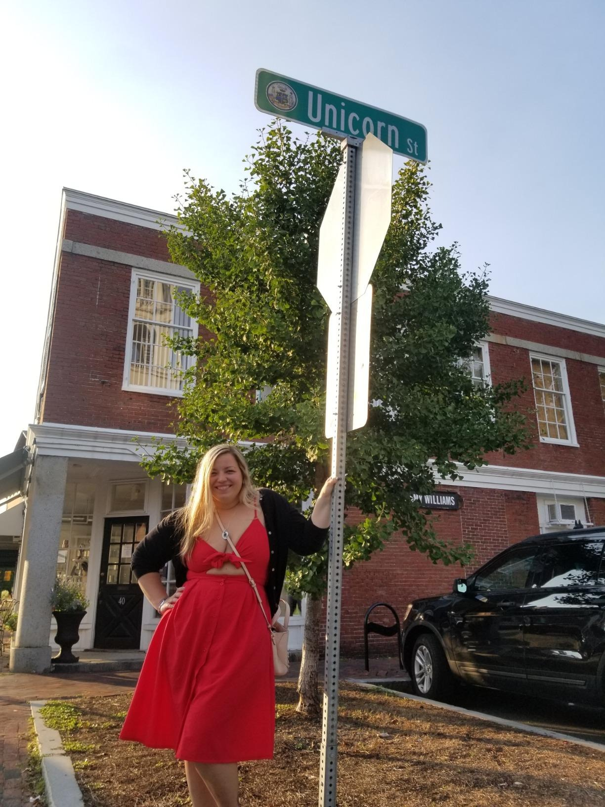 Person successful  a reddish  formal  poses adjacent  to a motion   for Unicorn Street with a smile, lasting  connected  a sidewalk successful  beforehand   of a ceramic  building