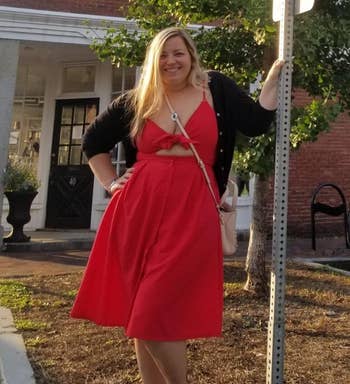 Person successful a reddish formal poses adjacent to a motion for Unicorn Street with a smile, lasting connected a sidewalk successful beforehand of a ceramic building