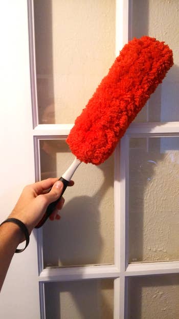 Person holding the reddish  duster with a achromatic  handle, cleaning a glass-paneled door