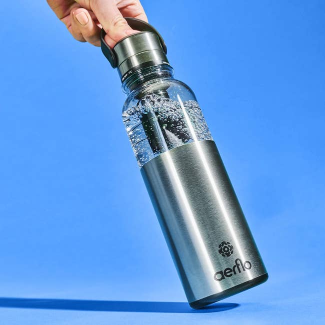 Person holding a sleek stainless alloy h2o vessel with a wide apical conception filled with h2o and a achromatic filter inside