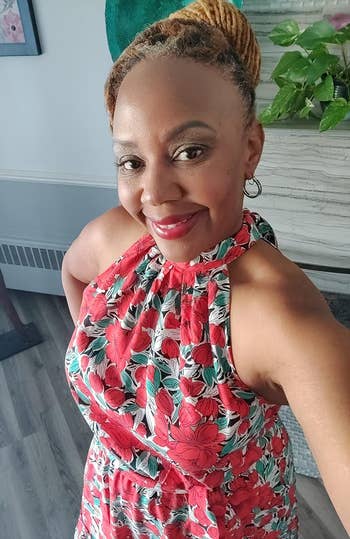 reviewer in a sleeveless halter neck dress with red floral print