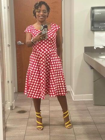 Reviewer in a red polka dot dress and yellow strappy heels posing for a take into accout selfie